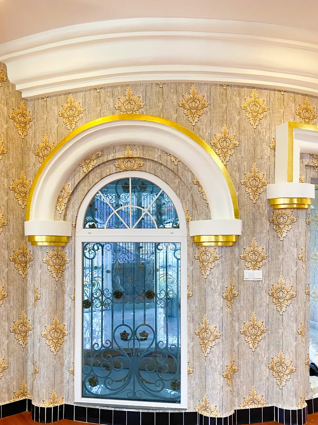 Gold damask MK wallpaper around a gilded arched window, Phnom Penh